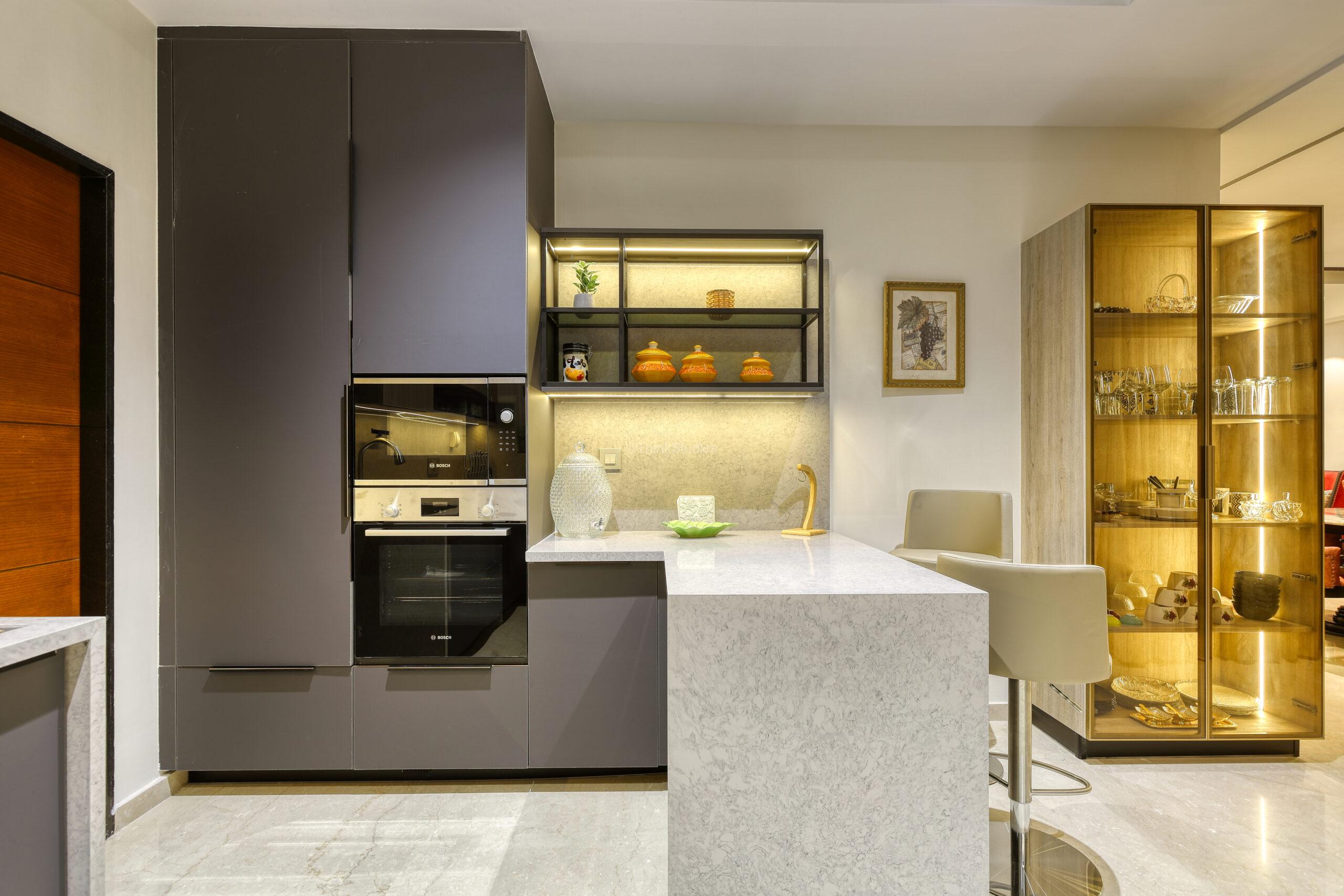 Shows a kitchen space, tastefully designed with a crockery cabinet, a small island, and accessible pantry as well as appliances.